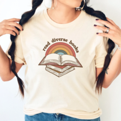 Read Diverse Books T-Shirt - A female model wears a round neck cream t-shirt with a rainbow and books retro-style printed design. Around the top of the rainbow is the text "read diverse books".