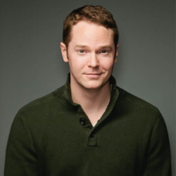 About the author Robert Jackson Bennett - A headshot of a white skinned man with short brown hair standing against a grey background. He is wearing a dark collared top and is facing the camera. The photo is cropped to show his head and shoulders.