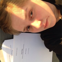 About the author: Kara Jorgensen - A white woman is laying on the floor with her head next to a pile of papers. She has light brown hair, and is wearing a dark top. The image is cropped to show her head and shoulders.