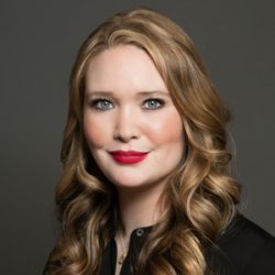 About the author: Sarah J. Maas - a white woman with long curly blonde hair standing against a dark background. She has blue eyes and is wearing red lipstick and a black top. The image is cropped to show her head and shoulders.